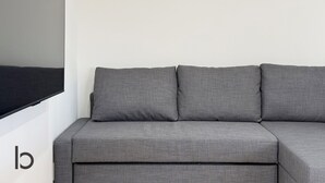 A grey sofa against a plain wall with a large black object on the left. - Lafort Honkawa (Hiroshima City)