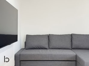 A grey sofa against a plain wall with a large black object on the left. - Lafort Honkawa (Hiroshima City)
