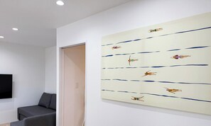 A room with a large abstract painting on the wall, a gray sofa, and a closed door. - Lafort Honkawa (Hiroshima City)