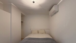 A bedroom with a bed, an air conditioning unit, and a light fixture on the ceiling. - Lafort Honkawa (Hiroshima City)