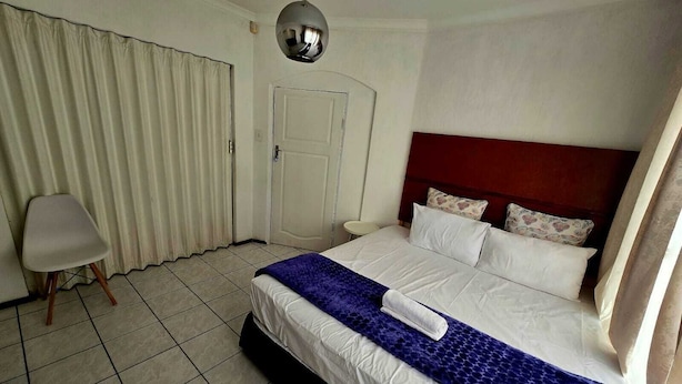 A hotel room with a bed, a chair, a door, and a mirror. - Room-charming Lodge Room in Sandton With (Johannesburg)