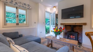 Una sala de estar con un sofá, una mesa con un florero, una chimenea y un televisor montado en la pared.