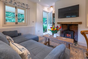 En stue med en sofa, et bord med blomster, en pejs og et tv ophængt på væggen.