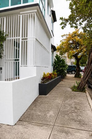 Ein modernes Gebäude mit weißer Fassade, einem schmalen Bürgersteig und einem Baum mit gelben Blättern.