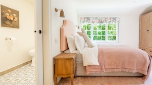 A bedroom with a bed, bedside table, and a window with a view of greenery. - Exceptional woodland cottage in Constable Country - Cosgrove Lodge (Colchester)