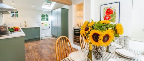 Ein Essbereich mit einem Tisch für vier Personen, einer Vase mit Sonnenblumen und einer Küche im Hintergrund.