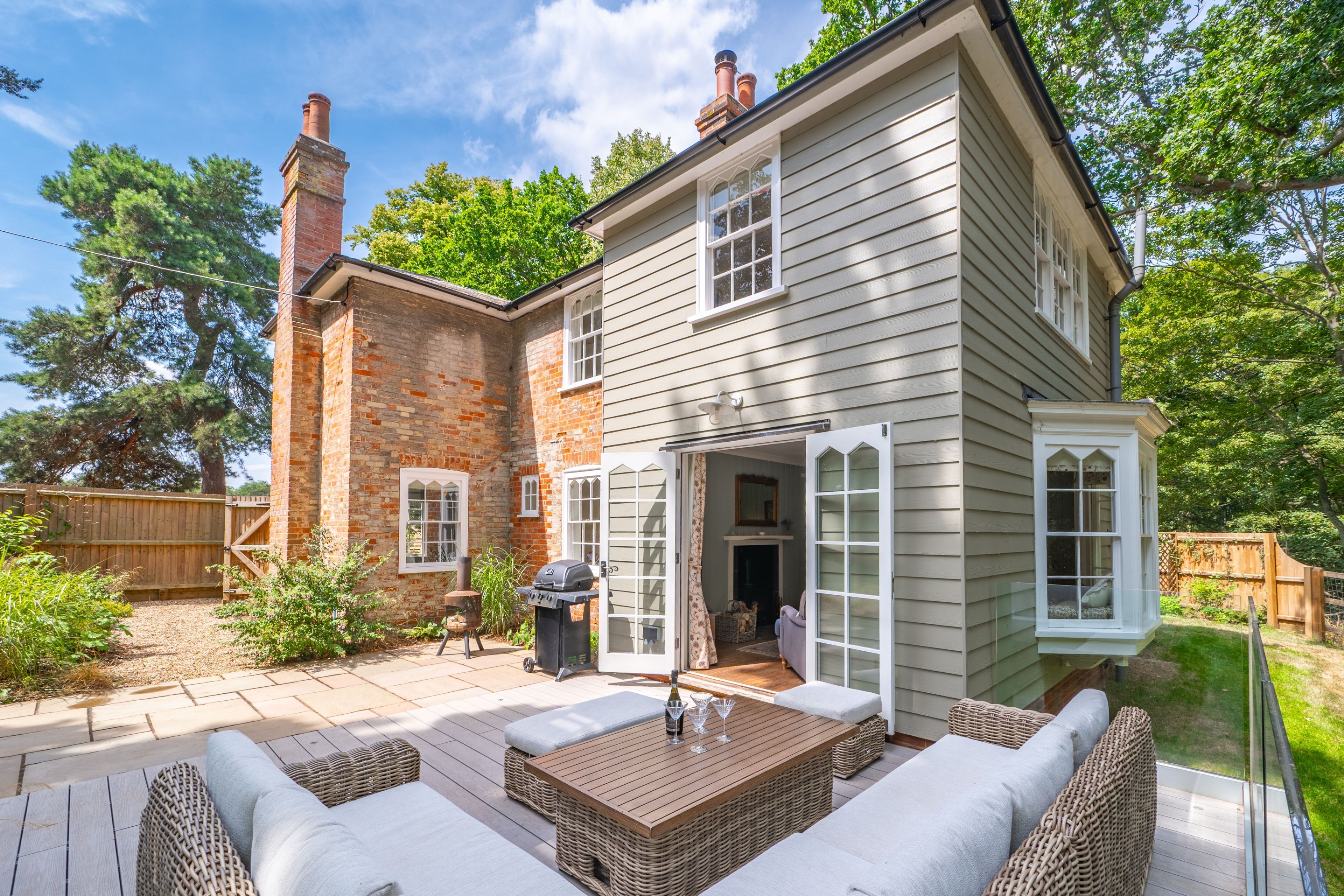 A two-story house with a brick chimney, a patio with wicker furniture, and a large window.