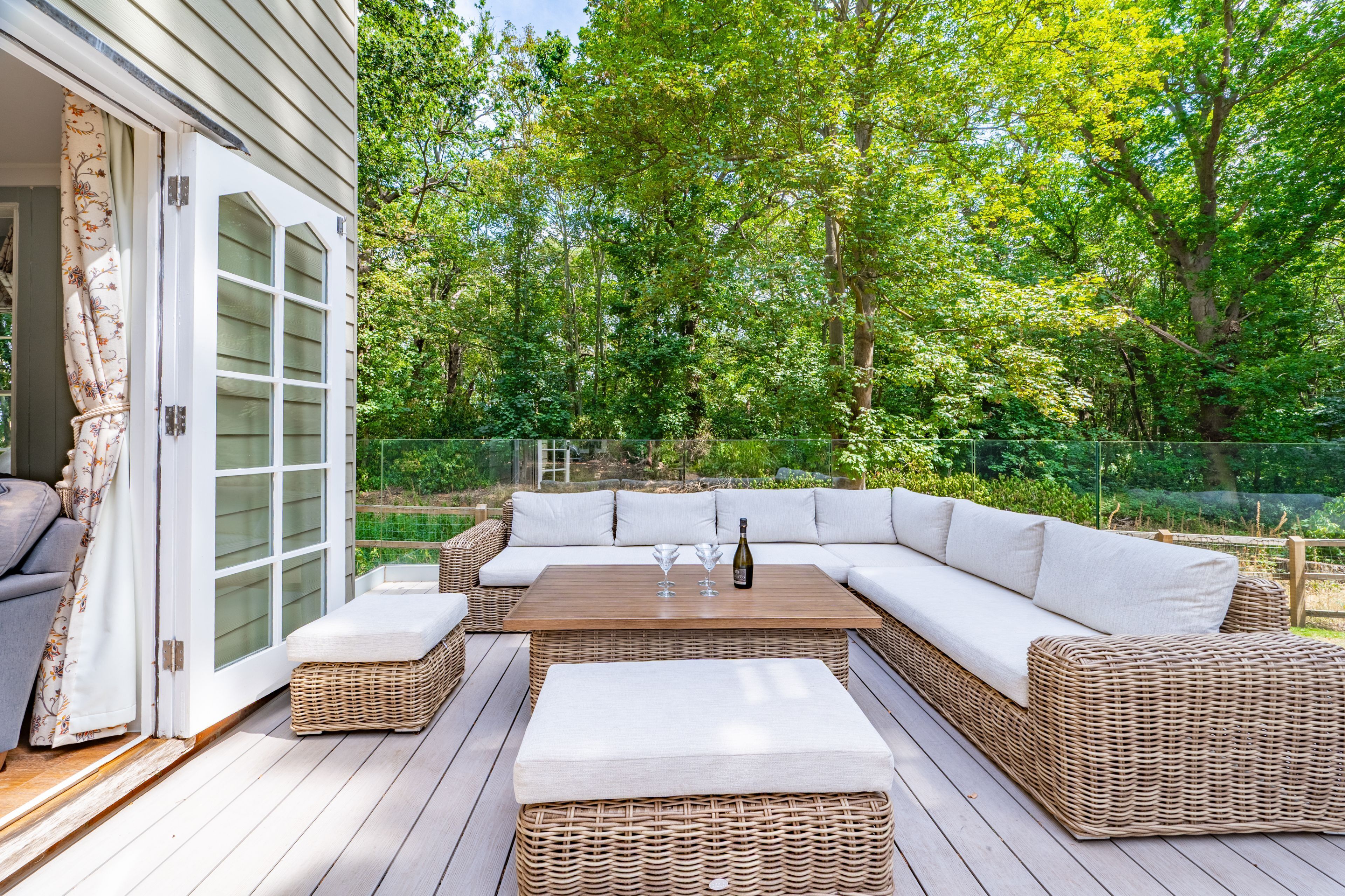 Eine Terrasse im Freien mit einer Eckcouch, einem Holztisch und einer Weinflasche.