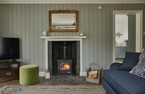 Ein Wohnzimmer mit Kamin, Fernseher, einem grünen Ottomanen und einem blauen Sofa.