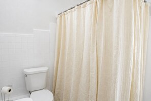 Ein Badezimmer mit Toilette, einer Toilettenpapierrolle und einem cremefarbenen Duschvorhang.