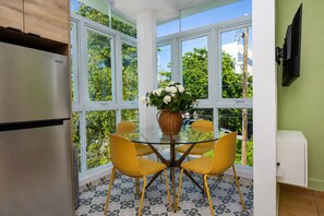 Eine Küche mit Kühlschrank, einem Esstisch mit Stühlen und einem Fenster mit Blick auf Grünflächen.