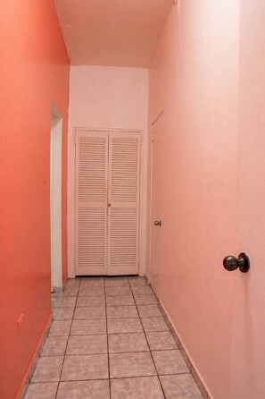 Un corridoio con una porta chiusa in fondo, pavimento piastrellato e pareti di colore chiaro.