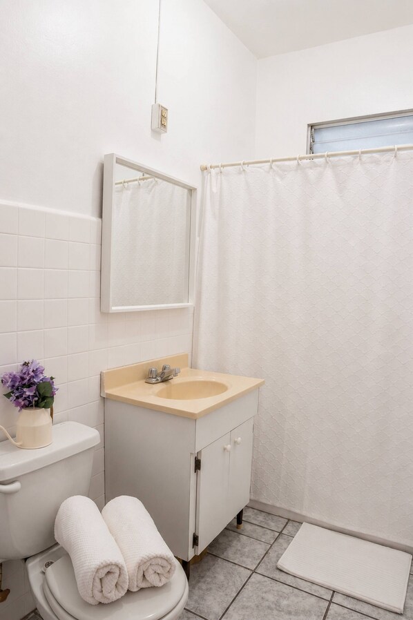 Un bagno con il water, lavandino, specchio e tenda per la doccia.