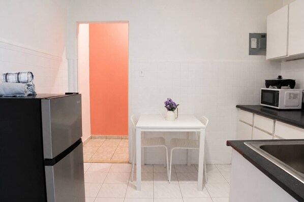 A compact kitchen with a refrigerator, microwave, and a small dining table with chairs. - Cozy 1 Bedroom Walk to Beach and Old San Juan (San Juan)