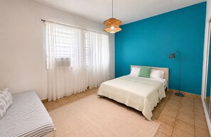 Ein Schlafzimmer mit einem Bett, einem Nachttisch, einer Lampe, einem Fenster mit Vorh ängen und einer blauen Akzentwand.