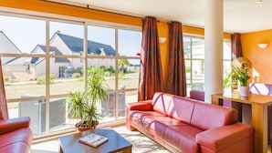 Una habitación de hotel moderna con un ventanal grande, un sofá de cuero rojo, una mesita pequeña y una planta en maceta.