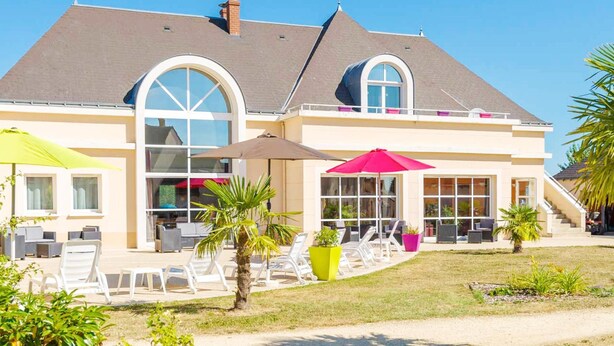 Una casa de dos pisos con un amplio patio, mobiliario exterior y una zona techada.