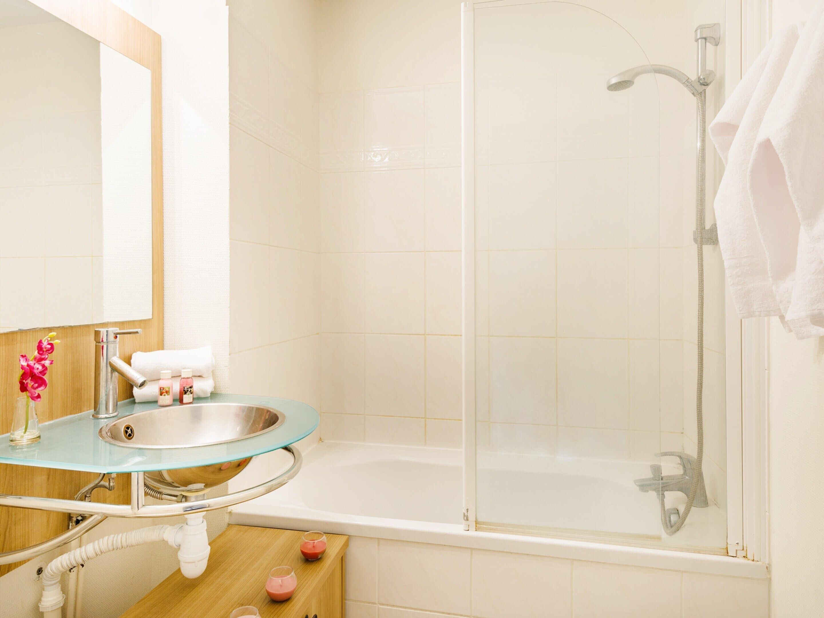 Een badkamer met een glazen wastafel, een badkuip en een douche.