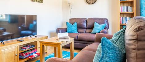 A living room with a brown leather sofa, a wooden coffee table, a bookshelf, and a wall clock.