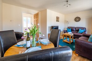 A dining area with a wooden table set for four, surrounded by leather chairs. A vase with flowers and a bottle of wine are on the table. - Seabreeze, Wells-next-the-Sea, Norfolk (Wells-next-the-Sea)