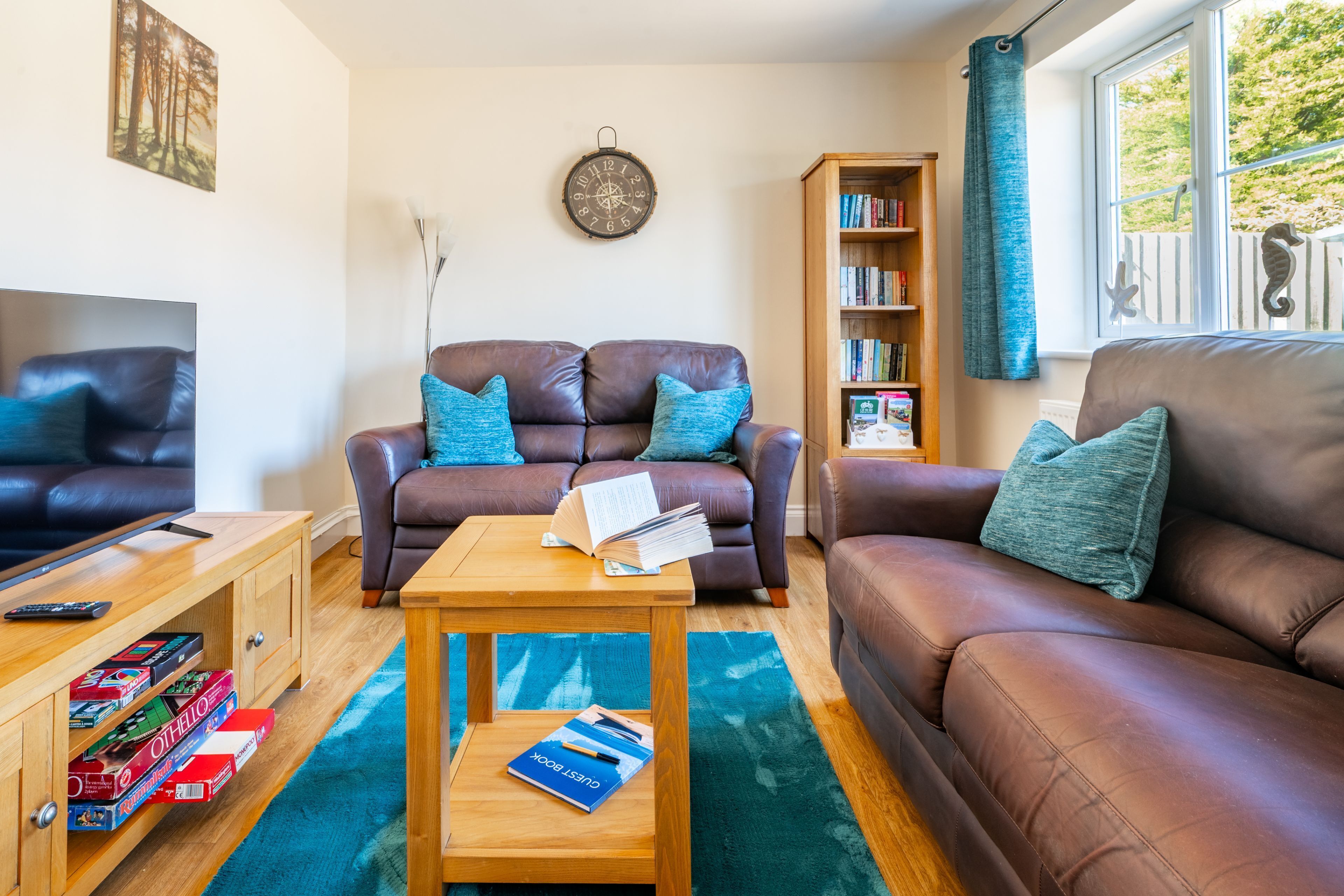 A living room with two brown leather sofas, a wooden coffee table, a bookshelf, and a window with curtains.