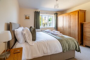A bedroom with a bed, a wooden wardrobe, a bedside table with a lamp, and a window with curtains. - Seabreeze, Wells-next-the-Sea, Norfolk (Wells-next-the-Sea)