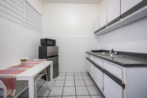 Eine kleine Küche mit weißen Schränken, einem Edelstahlkühlschrank, einer Mikrowelle und einem Spülbecken.