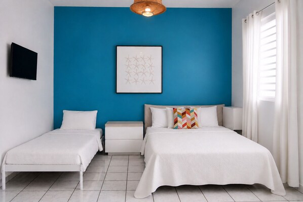 Una camera da letto con due letti, una parete di colore blu, un quadro appeso e una televisione a parete.