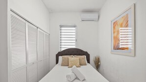 A bedroom with a bed, white walls, a window with blinds, a ceiling fan, and a framed picture. - Cozy Family Apartment at San Juan (San Juan)