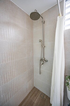 A shower with a handheld showerhead, a wall-mounted faucet, and a white towel hanging on a rack. - Stylish and Comfortable Studio Steps from La Cerra (San Juan)
