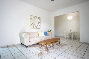 A living room with a sofa, a coffee table, a dining table with chairs, and a chandelier. - Budget Friendly Apt with 2 Balconies Near Beach (San Juan)