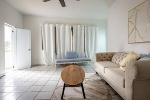 A living room with a sofa, a round coffee table, a white door, and a curtain. - Budget Friendly Apt with 2 Balconies Near Beach (San Juan)