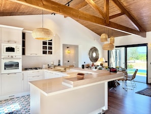 A modern kitchen with white cabinetry, a large island, and a dining area with wicker chairs.