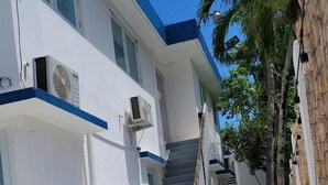 A white building with a blue trim, a staircase, and a palm tree.
