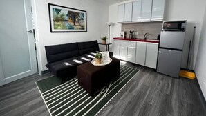A compact living space with a sofa, a small table with a plant, a kitchen area with cabinets and a microwave, and a framed picture on the wall.