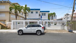 A white SUV parked in front of a gated residential area with a blue and white building in the background.
