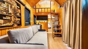 A cozy cabin interior with a sofa, wooden shelves, a kitchen area, and a loft space. - Elite Escape Village Hotel (Catalca)