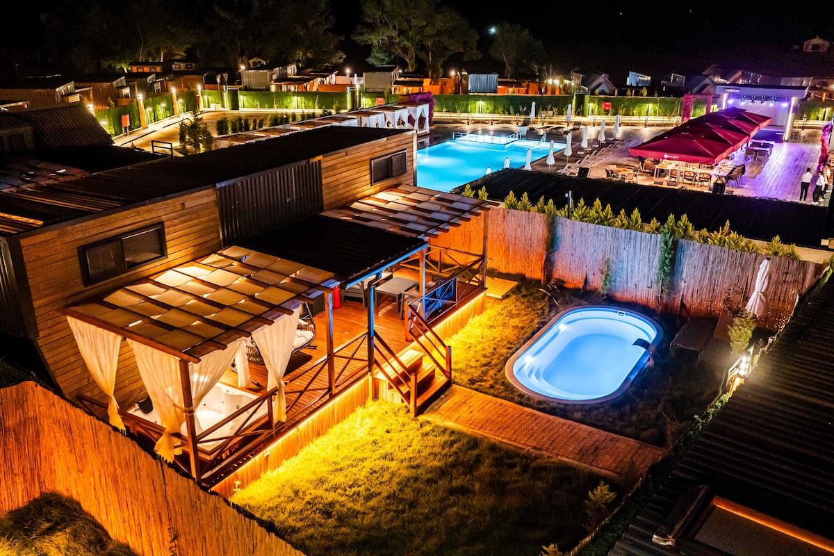 A well-lit outdoor area with a swimming pool, a hot tub, and a covered seating area.