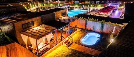 A well-lit outdoor area with a swimming pool, a hot tub, and a covered seating area.
