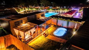 A well-lit outdoor area with a swimming pool, a hot tub, and a covered seating area.