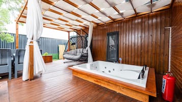 A wooden deck with a hot tub, a hanging chair, and a fire extinguisher.