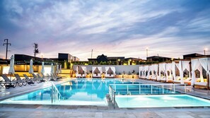 A swimming pool with sun loungers and canopy tents, surrounded by buildings and a clear sky.