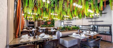An indoor restaurant with hanging plants, wooden ceiling beams, and tables set for dining.