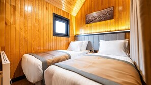 A wooden-paneled room with two beds, a window, and a painting on the wall.