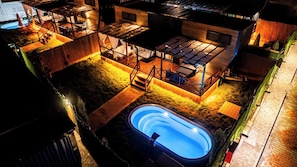 Un área de piscina en la azotea con jacuzzi, terraza de madera y mobiliario exterior.