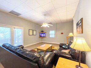 A living room with a black leather sofa, a wooden coffee table, a TV on a stand, and a ceiling fan. - The Gathering Haus - 10% OFF or 4th Night Free - Ask for details! (Helen)