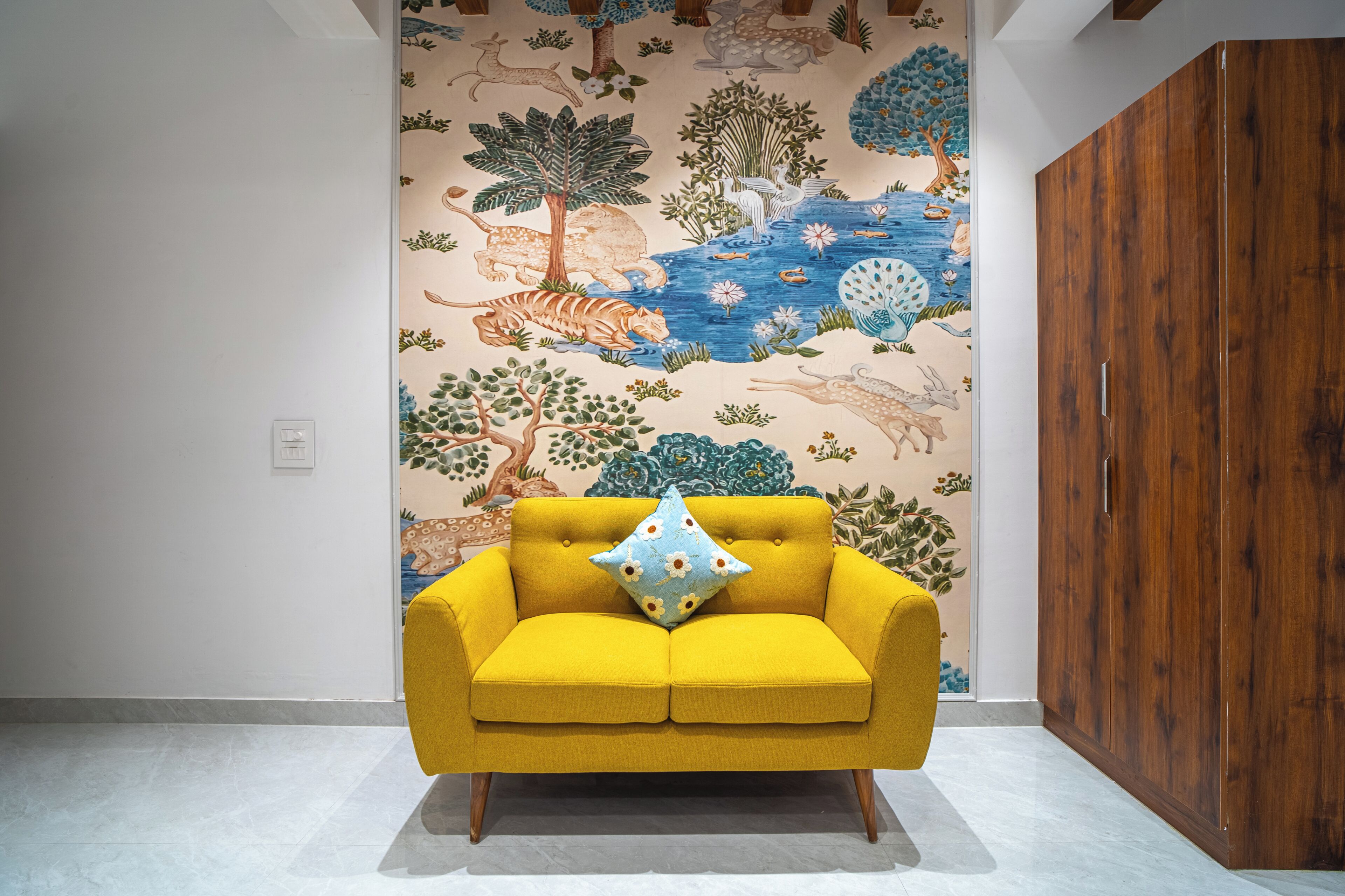 A yellow sofa with a floral pillow in a room with a mural of wildlife and nature.