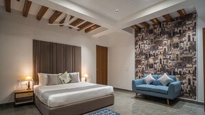 A modern hotel room with a large bed, a blue sofa, a patterned wall, and a ceiling fan. - Alaya Stays Udgam Villas 5BHK Apartment (Dehradun)