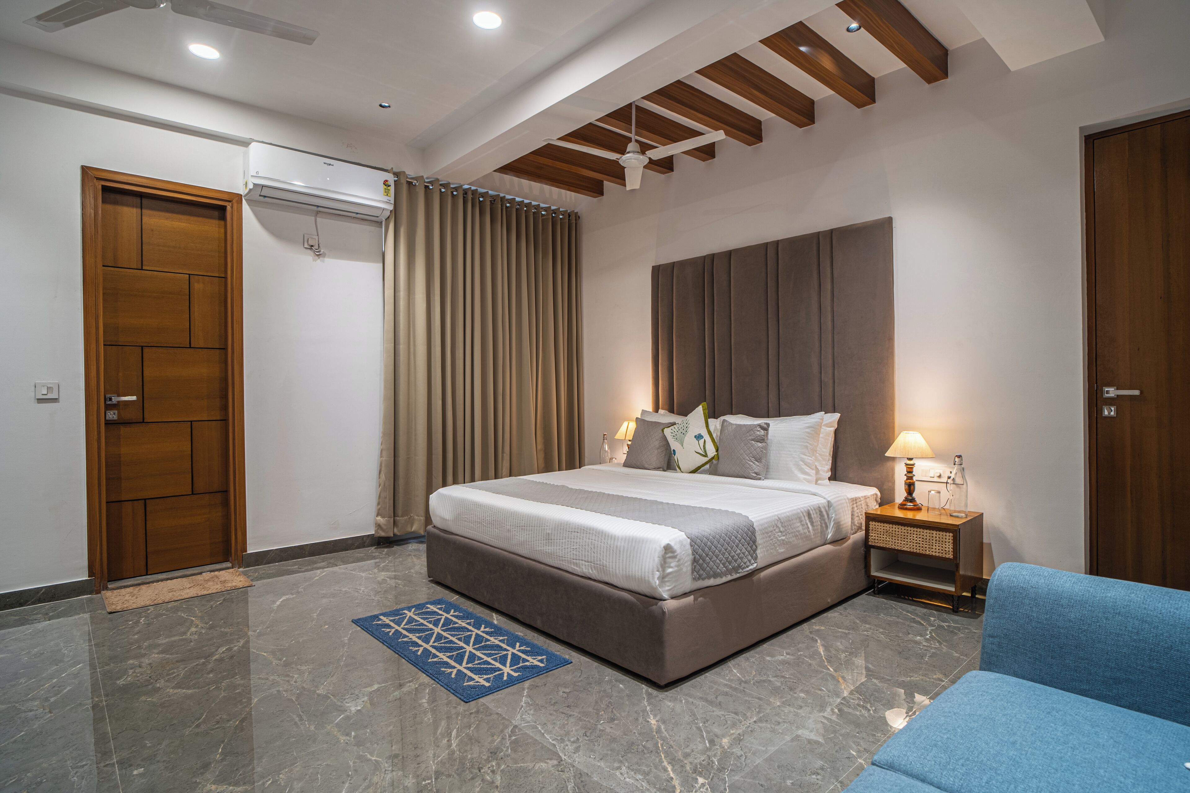 A bedroom with a bed, a nightstand, a blue sofa, a wooden door, and a ceiling fan.