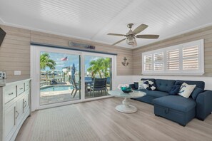 A living room with a blue sofa, a glass coffee table, and a ceiling fan. - Beachy 4 Bedroom 3 Bath Pool Home Mins to Redington Beach (Redington Beach)
